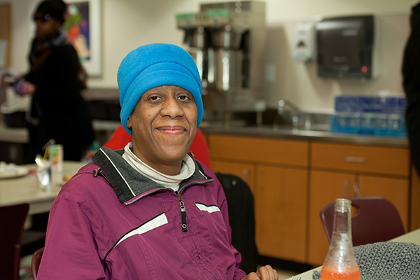 A woman smiles while eating at Angeline's Day Center