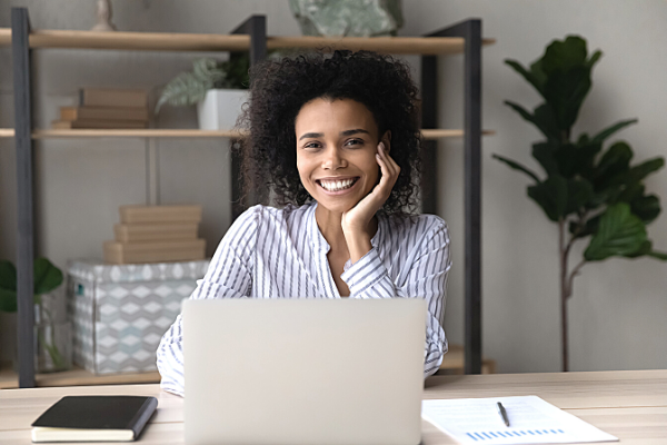 Black woman smiling and sitting in front of lap top