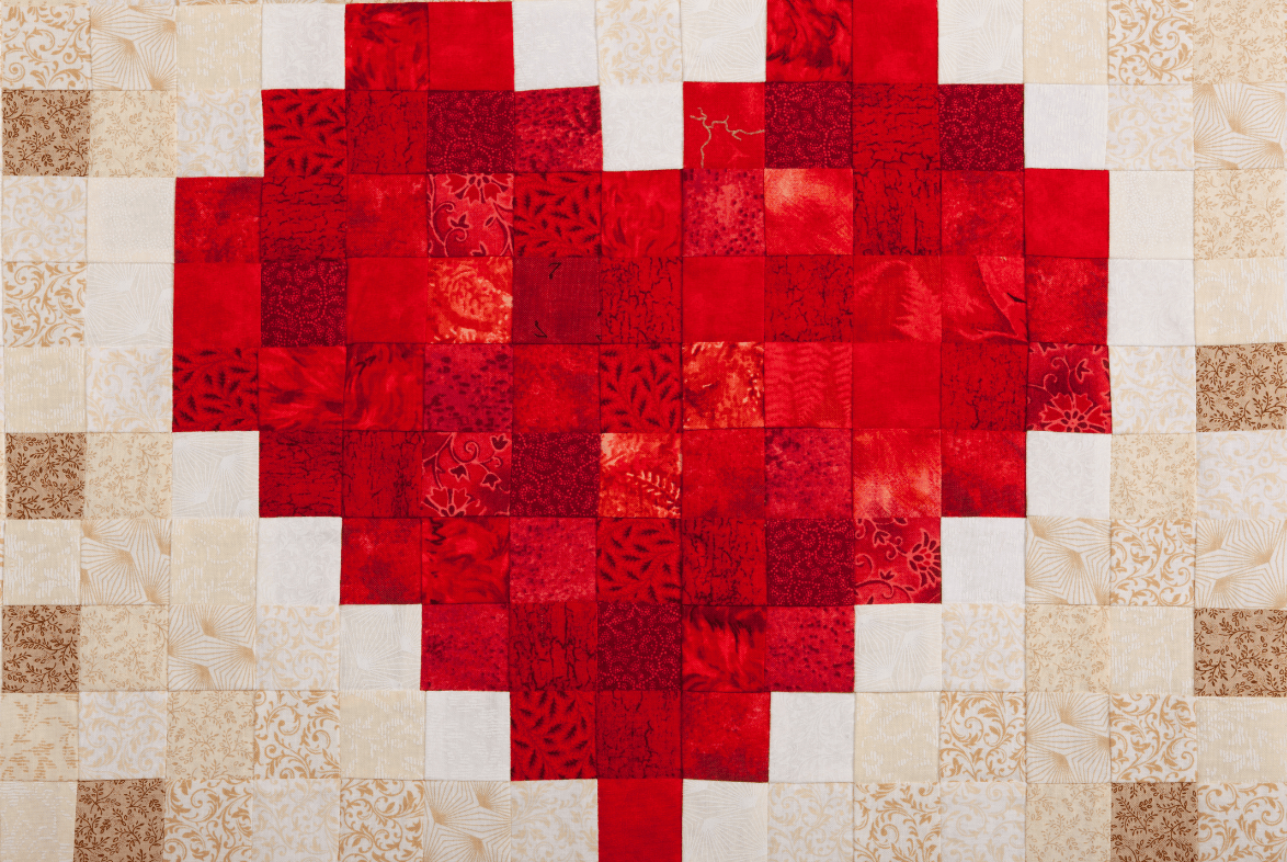 Photo of a quilt with a red heart design against a pale tan background