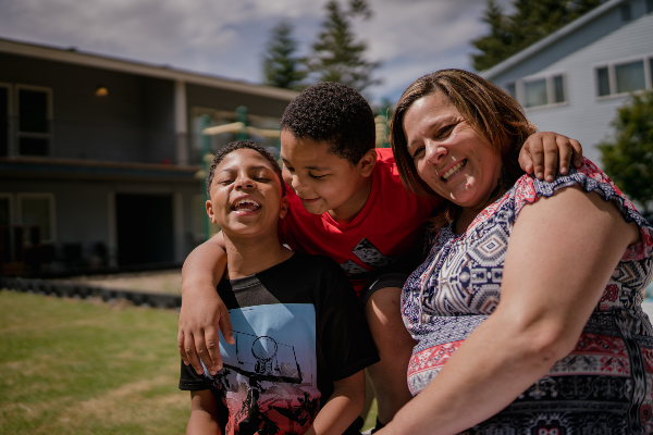 A woman and her sons pose in front of their home