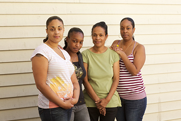 A Black woman and her family stand in front of their home