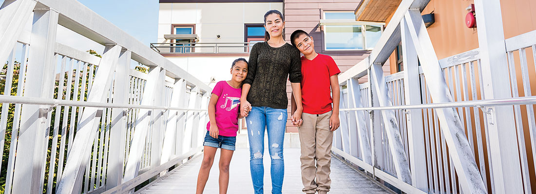 A mother and her two children standing in front of an apartment building.