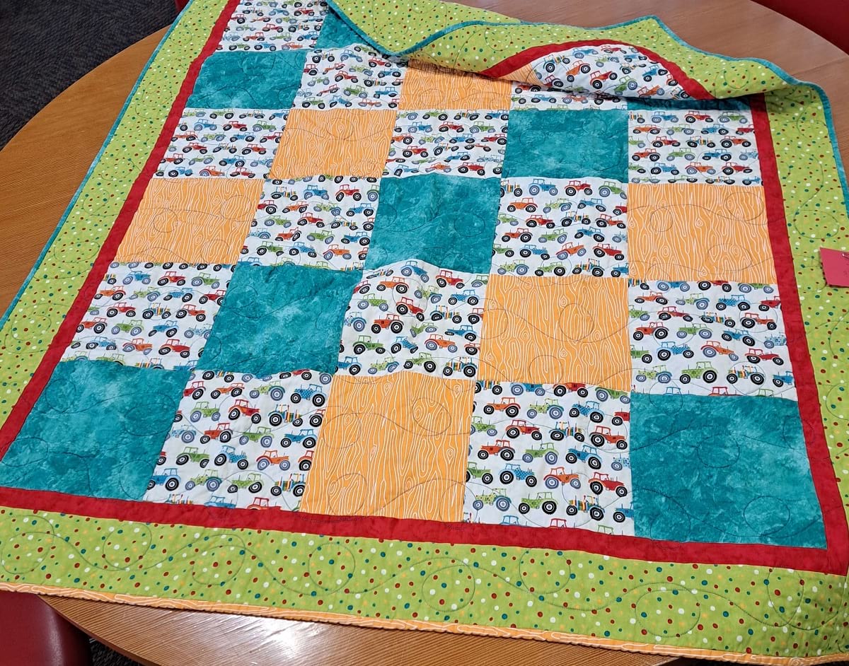 Photo of a multicolored green and white quilt lying on a table.