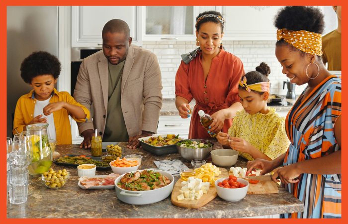 Photo of a family standing around a kitchen island cooking together.