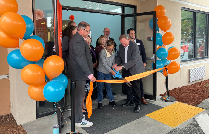 Event speakers cutting an orange ribbon with large blue scissors
