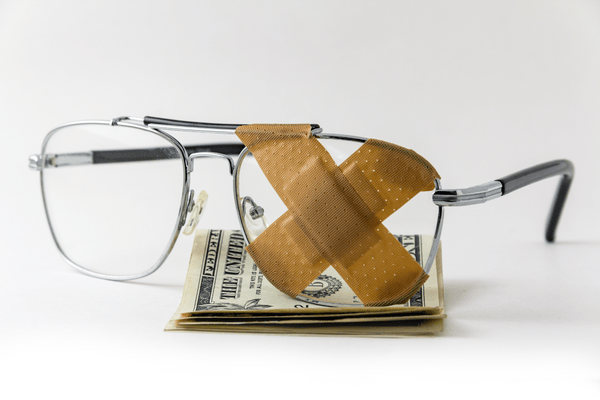 Photo of glasses sitting on folded dollar bills with bandages covering one frame.