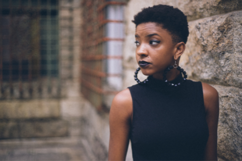 Picture of Black woman standing in front of a brick wall, looking away