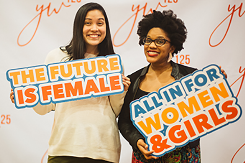 Two women holding signs that say "The future is female" and "all in for women and girls"
