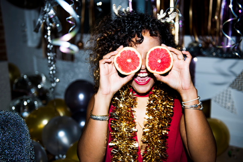Black woman at party using grapefruit as glasses