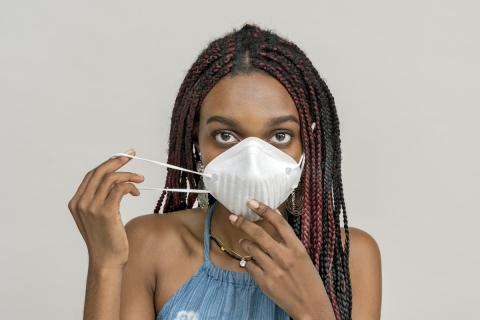 A Black woman puts on a face mask 