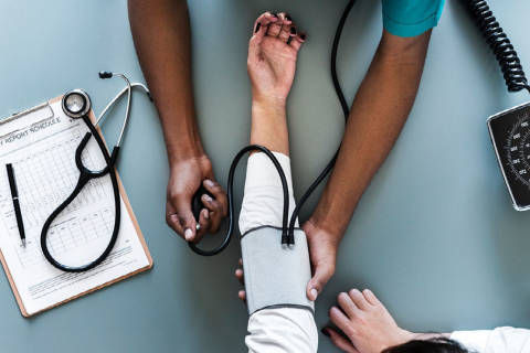 Picture of a Black medical provider's arms taking the blood pressure of a patient
