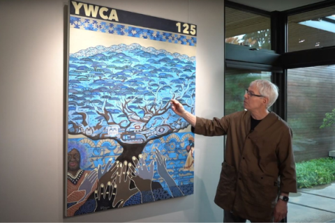 Photo of artist Spencer Frazer standing in front of original artwork inspired by YWCA, symbolized by a tree of life