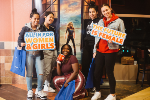 Picture of five girls at the Captain America screening holding signs that say "All in for women & girls" and "the future is female"