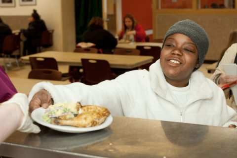 Photo of a black woman being served a plate of food at Angeline's Day Center