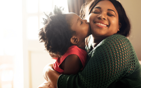 Black mother and child, joyfully making crafts on a wooden table.