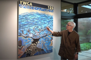 Photo of artist Spencer Frazer standing in front of original artwork inspired by YWCA, symbolized by a tree of life