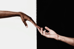 Half black half white image split down the middle with two hands reaching towards one another from opposite corners.