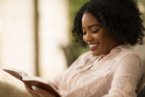 Photo of a black woman sitting down smiling and holding an open book